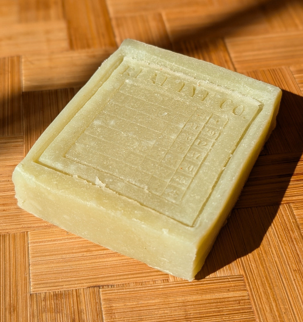 A rectangular bar of pale yellow soap with an embossed label reading 'MARTINE CO' sits on a warm-toned wooden surface under direct sunlight.