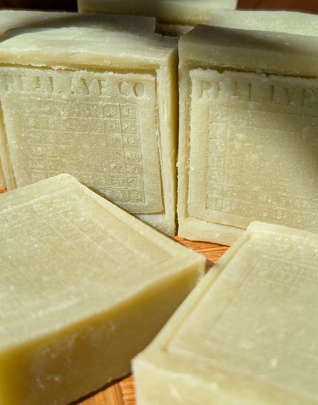 Several rectangular bars of pale yellow-green soap with embossed text reading 'REAL LYE CO.' arranged on a wooden surface.