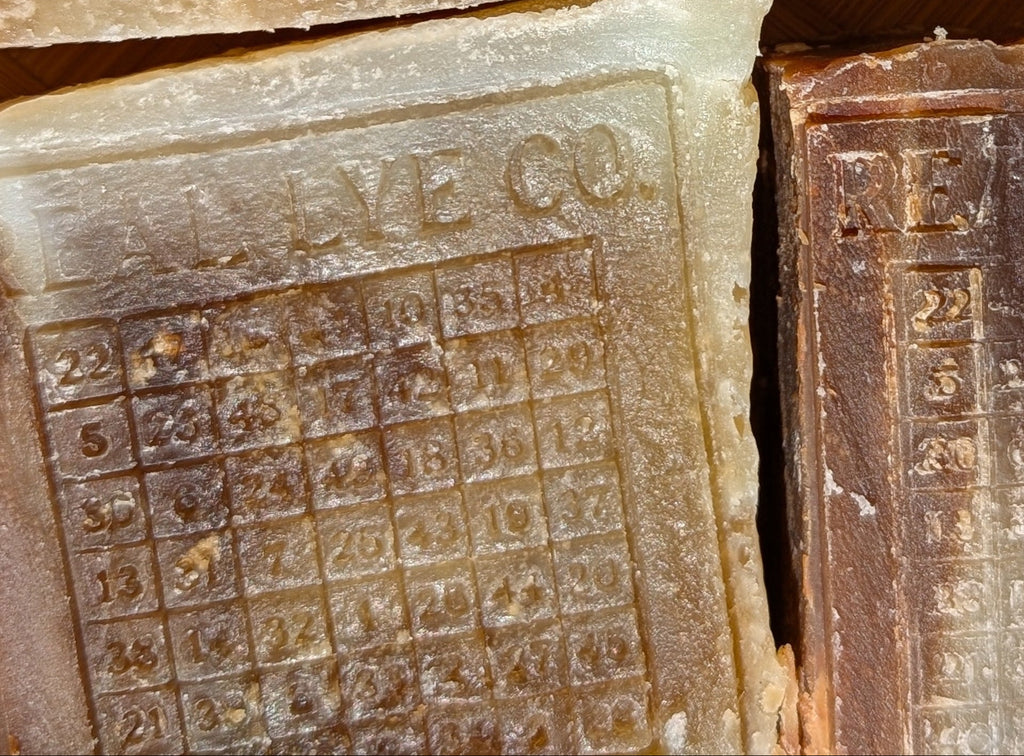 Four rectangular handmade soap bars stacked in a 2x2 grid, featuring a rustic marbled design of brown, beige, and olive green with embossed text and grid patterns on the front faces.