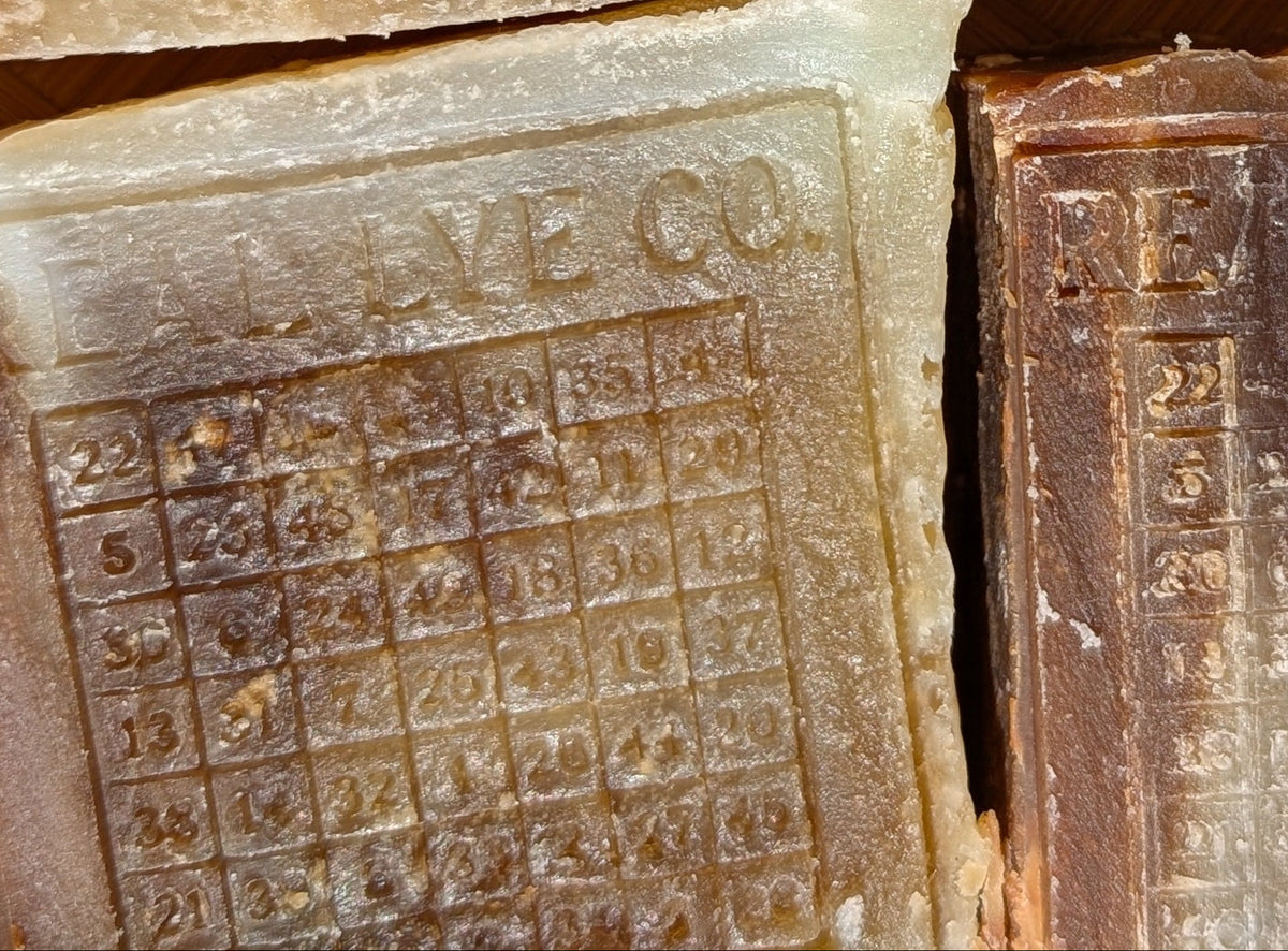 Four rectangular handmade soap bars stacked in a 2x2 grid, featuring a rustic marbled design of brown, beige, and olive green with embossed text and grid patterns on the front faces.