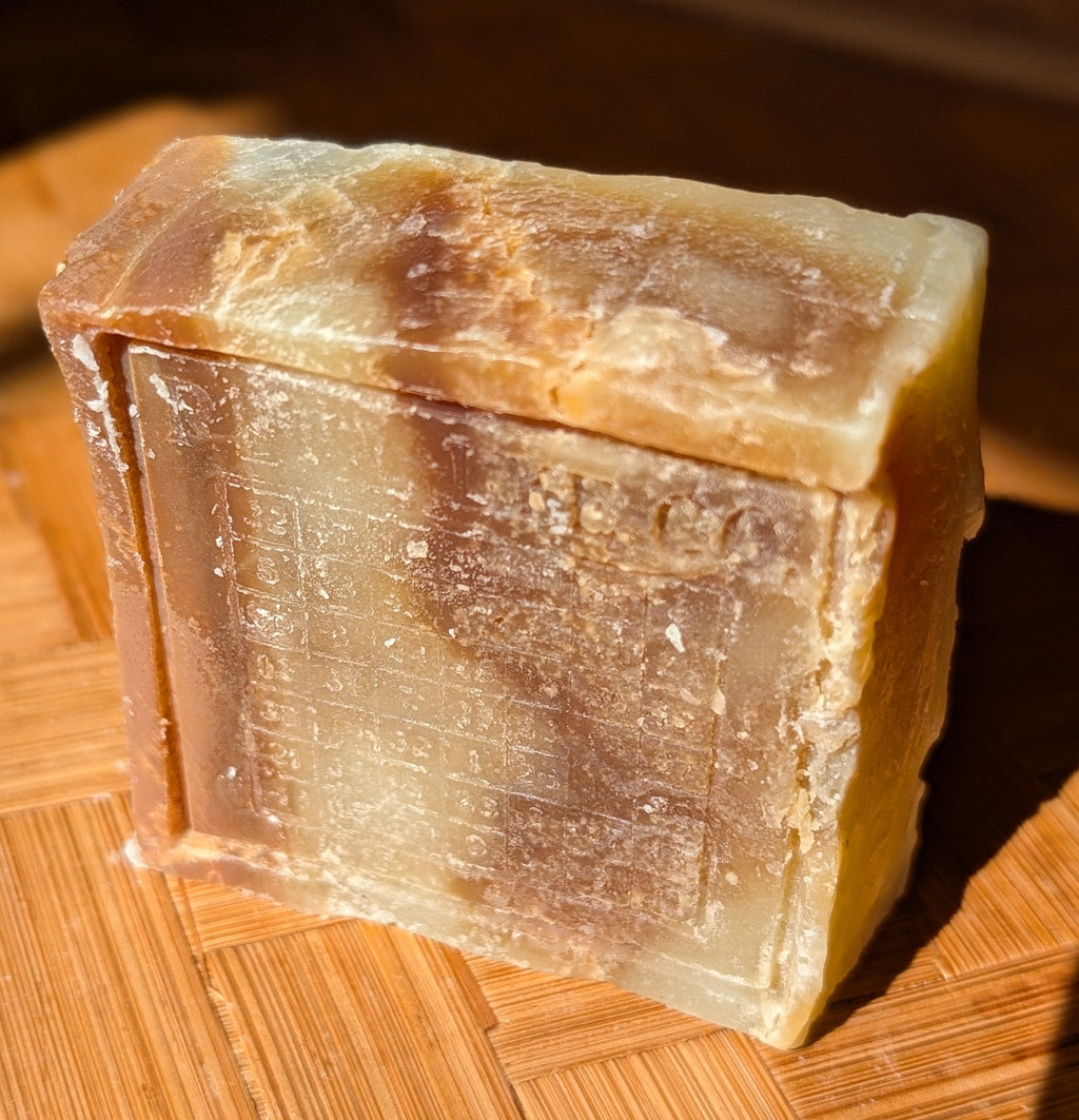 A rectangular bar of handmade soap with a marbled pattern of beige, brown, and translucent amber tones, resting on a wooden surface.