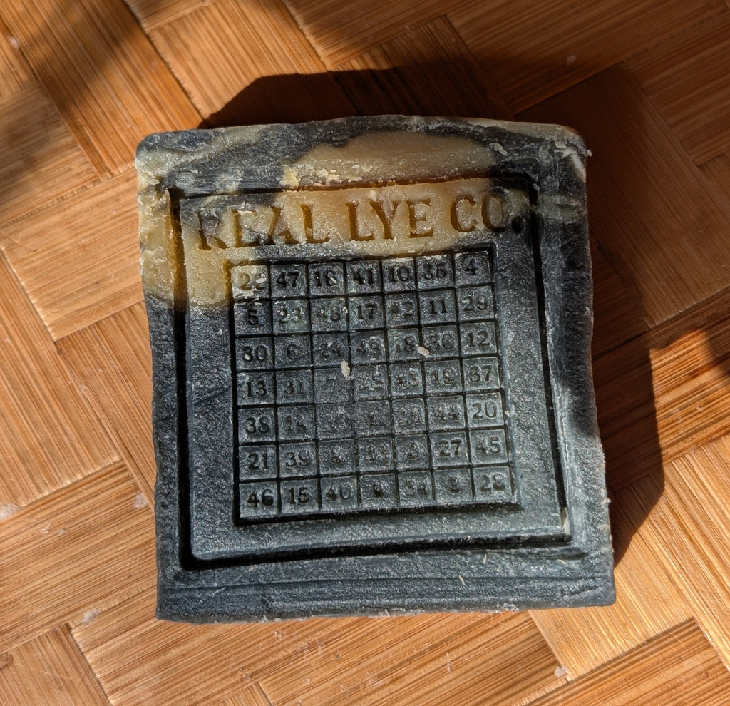 A vintage dark gray cast iron lye stone with 'REAL LYE CO' embossed at the top, resting on a wooden parquet floor.