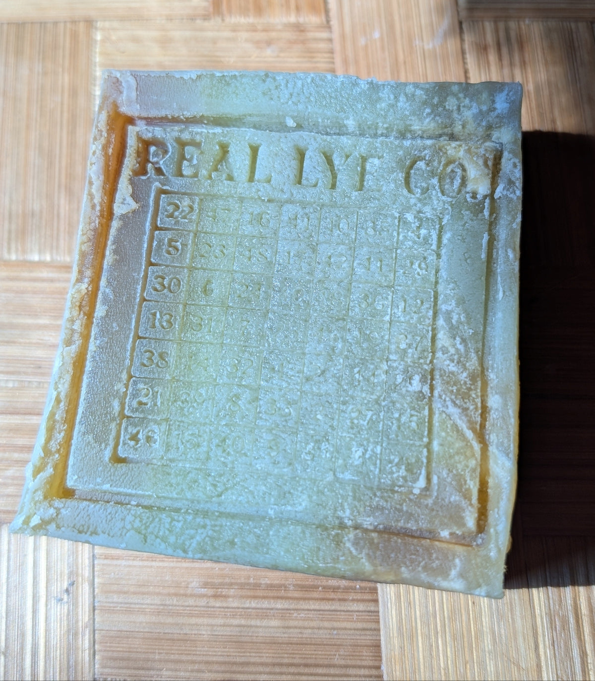 A rectangular bar of handmade soap with 'REAL LYT CO.' embossed on the top, resting on a bamboo-patterned surface.
