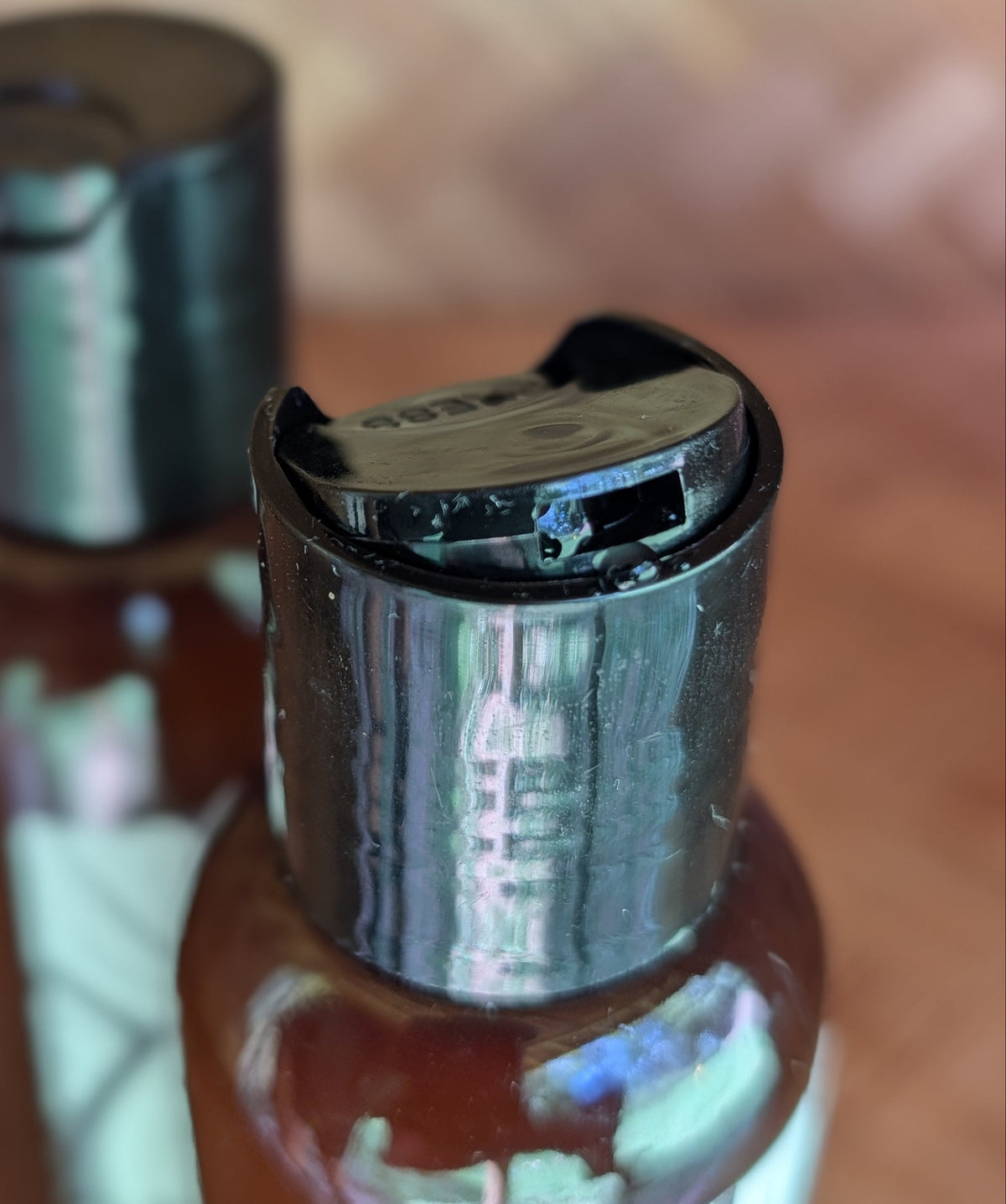 Two amber plastic bottles with black flip-top dispensers, photographed close-up on a wooden surface with a blurred background.