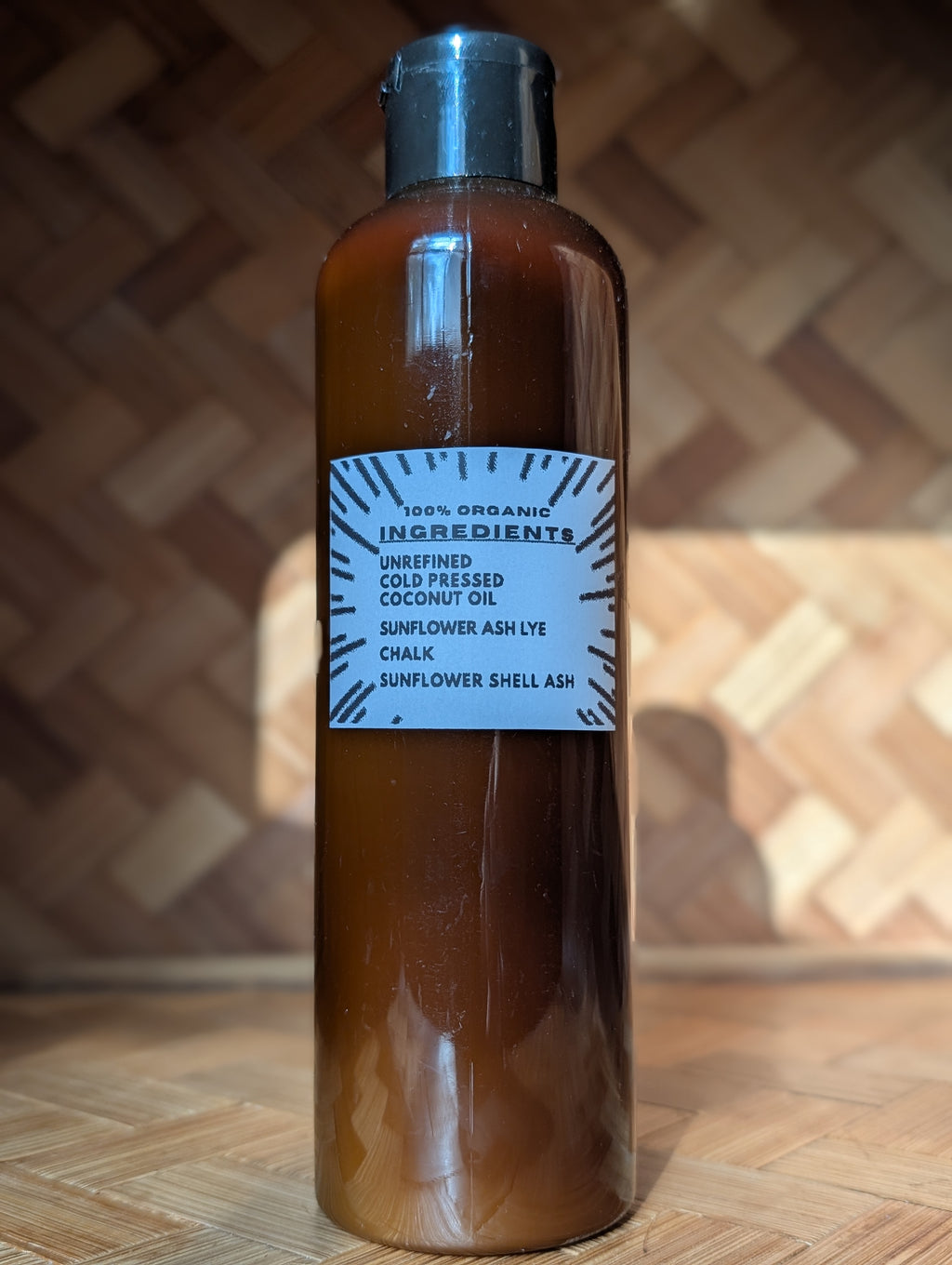 An amber glass bottle of cold pressed coconut oil with a black cap and a white label, set against a wooden background.