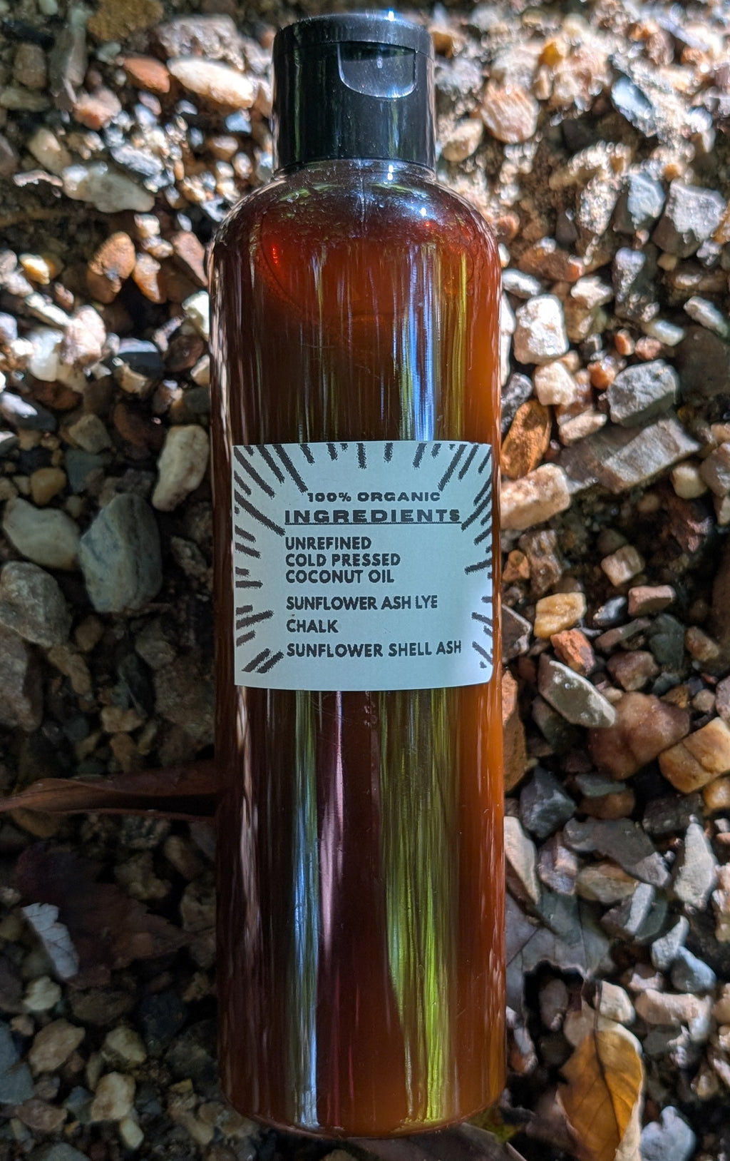 A bottle of cold-pressed sunflower oil with a black cap and a white label, placed on a bed of small brown and gray gravel.