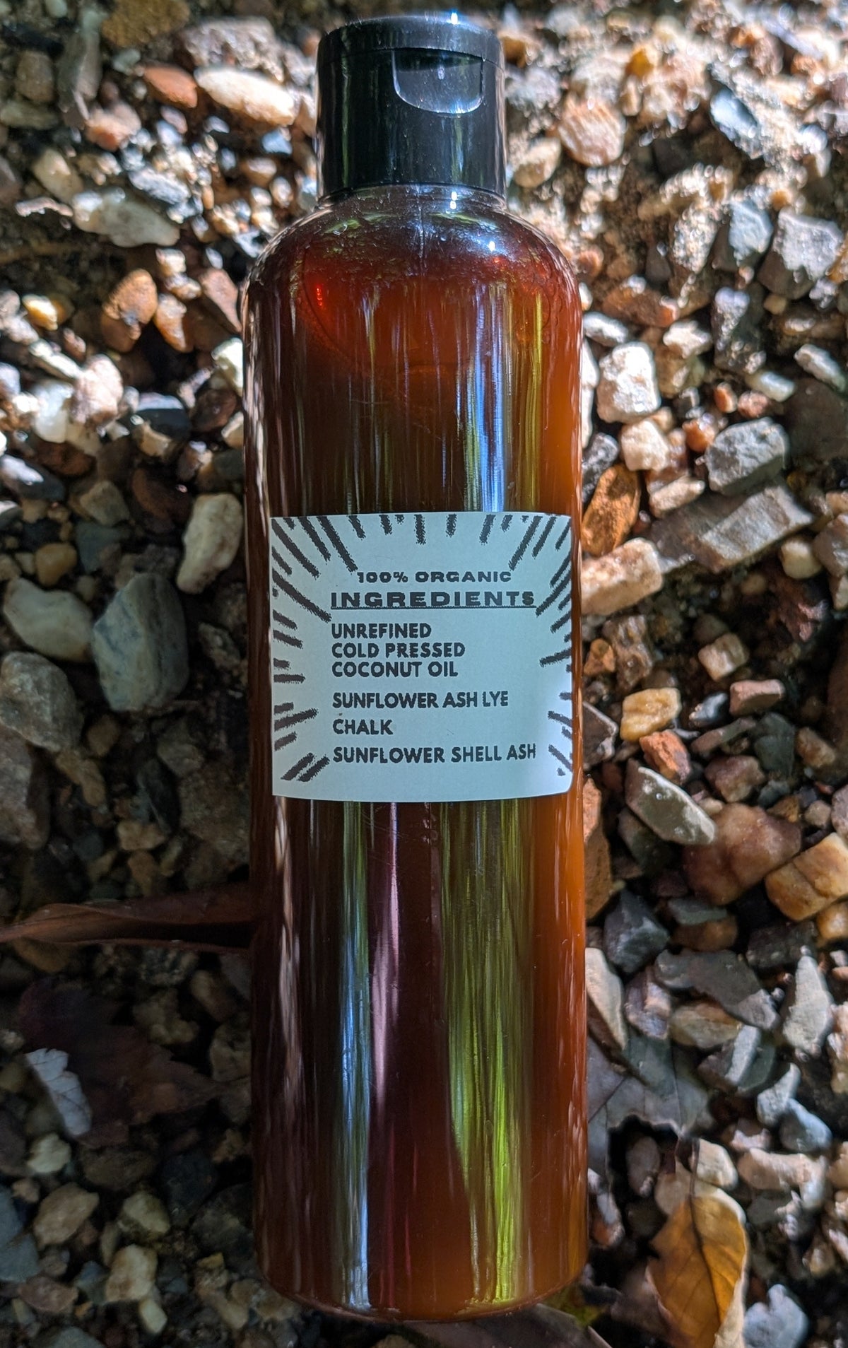 A bottle of cold-pressed sunflower oil with a black cap and a white label, placed on a bed of small brown and gray gravel.